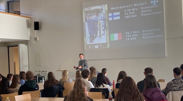 Junger Mann in Uniform vor einer Leinwand im Klassenraum